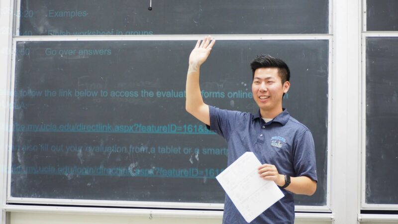 A UCLA instructor standing at the front of the class raising his hand to students