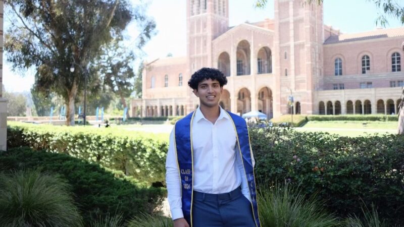 A photo of Anish Dulla posing with his graduation sash in front of UCLA's Royce Hall