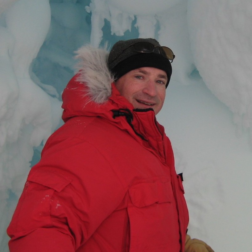 An image of professor David Saltzberg in a parka surrounded by ice during a research excursion 