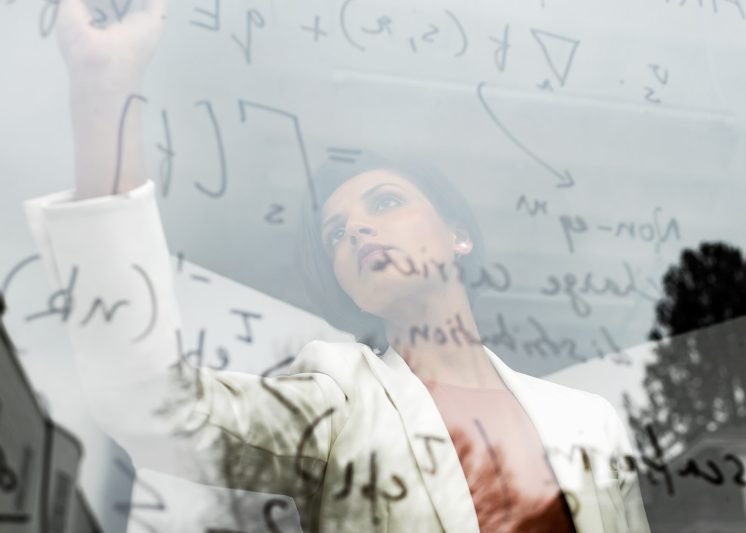 Pri Narang writing math equations on a glass whiteboard